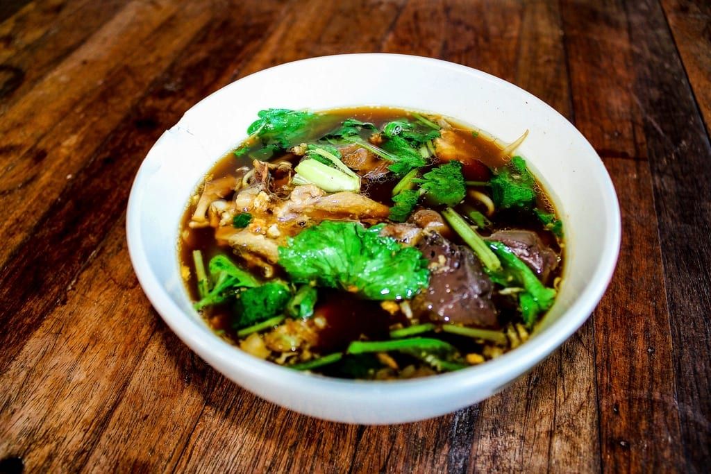 Beef noodle soup with greens in a white bowl