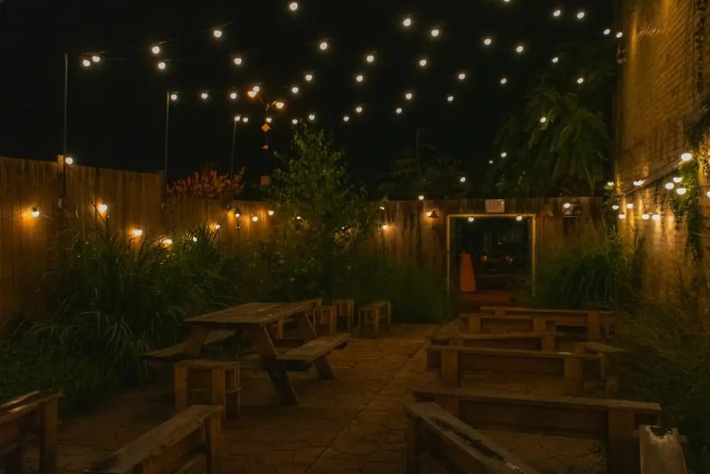 A courtyard patio with picnic tables under string lights at night