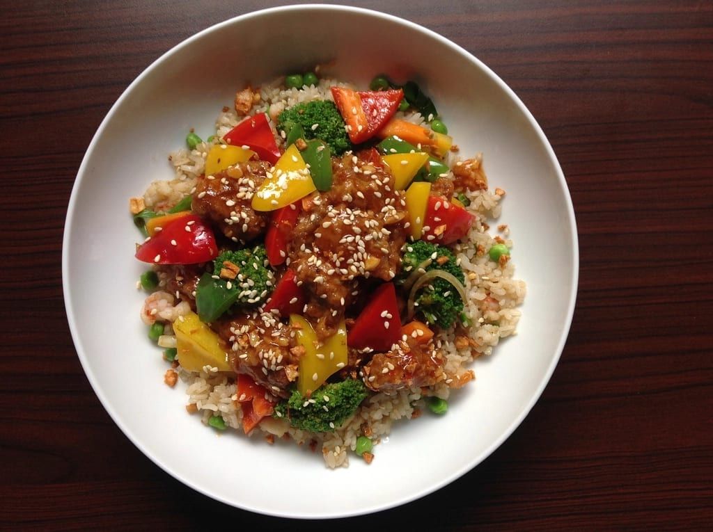Sesame-glazed chicken with peppers over rice in a white bowl