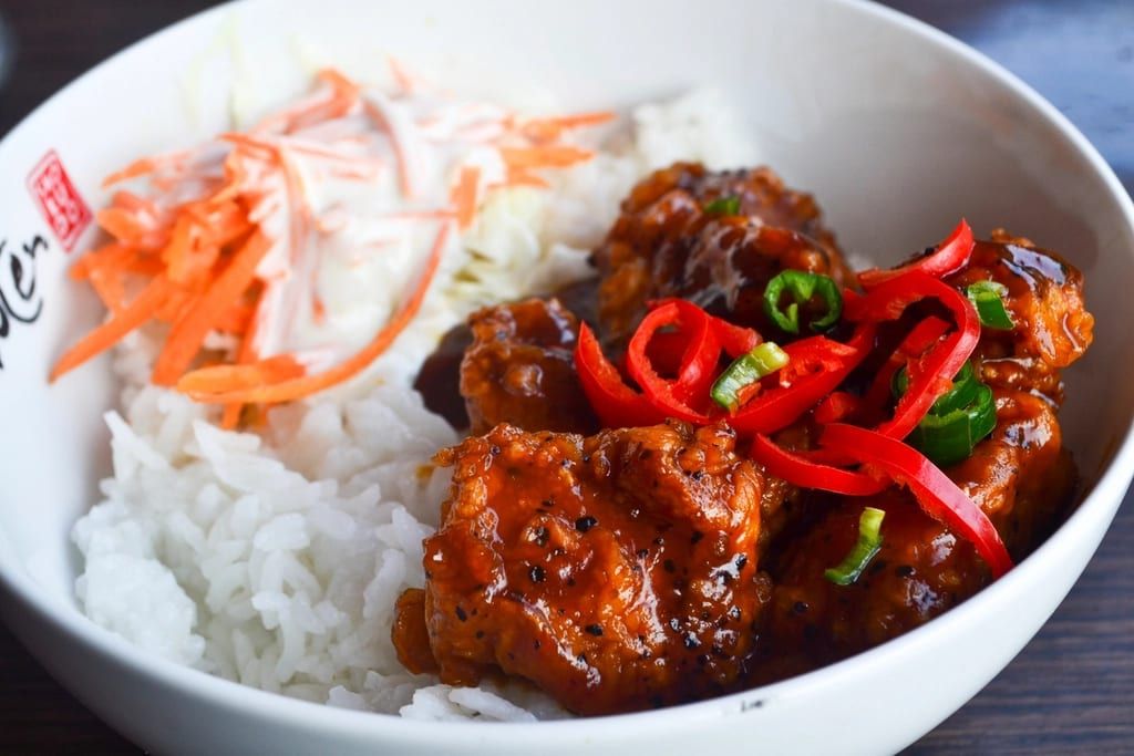 Glazed fried chicken with red peppers over rice with carrot slaw